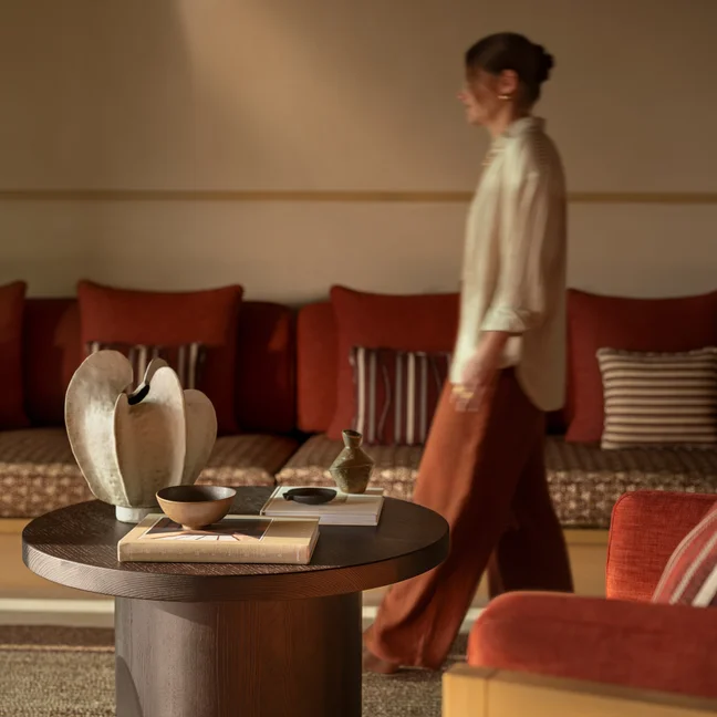 A modern living room with warm-toned sofas, striped cushions, and a round wooden coffee table displaying curated decor and books.