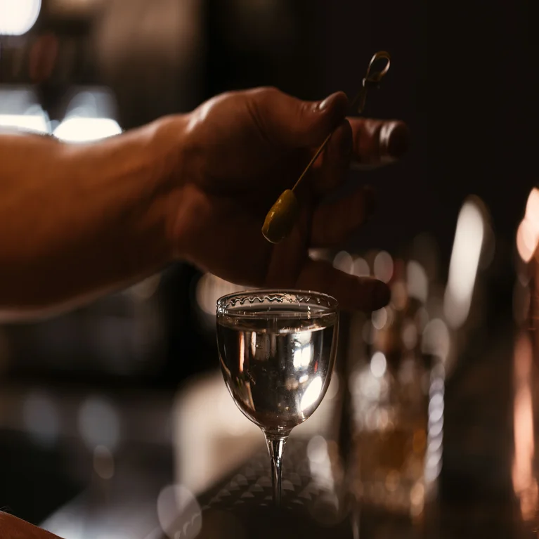 A single olive on a cocktail pick suspended over a clear drink.