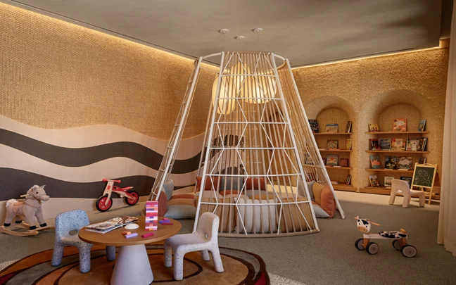 A playroom with a cone-shaped climbing structure, a table and chairs, a rocking horse, and wall-mounted bookshelves.