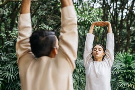 Les invités se tiennent debout, les bras levés et les yeux fermés, dans un cadre naturel de verdure vibrante, pour une séance de yoga en pleine conscience....