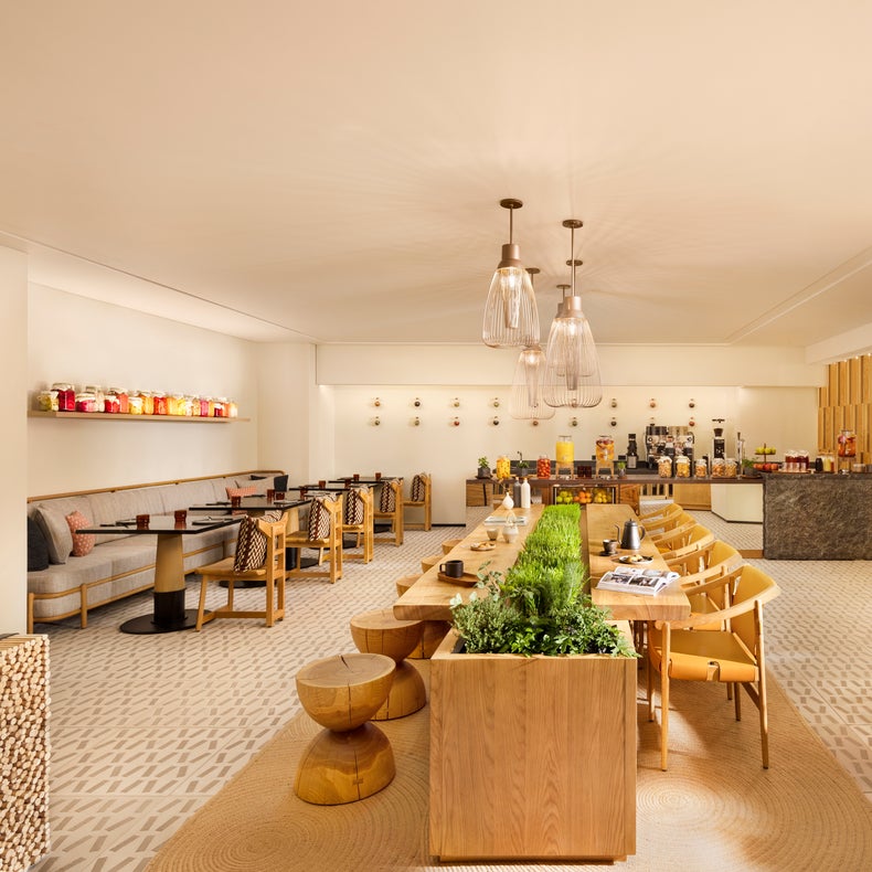منطقة لتناول الطعام مزودة بطاولات وكراسي خشبية، وقطع مركزية مغطاة بالخضرة وبوفيه وأضواء معلقة وألوان محايدة ومقاعد متباعدة بعناية.