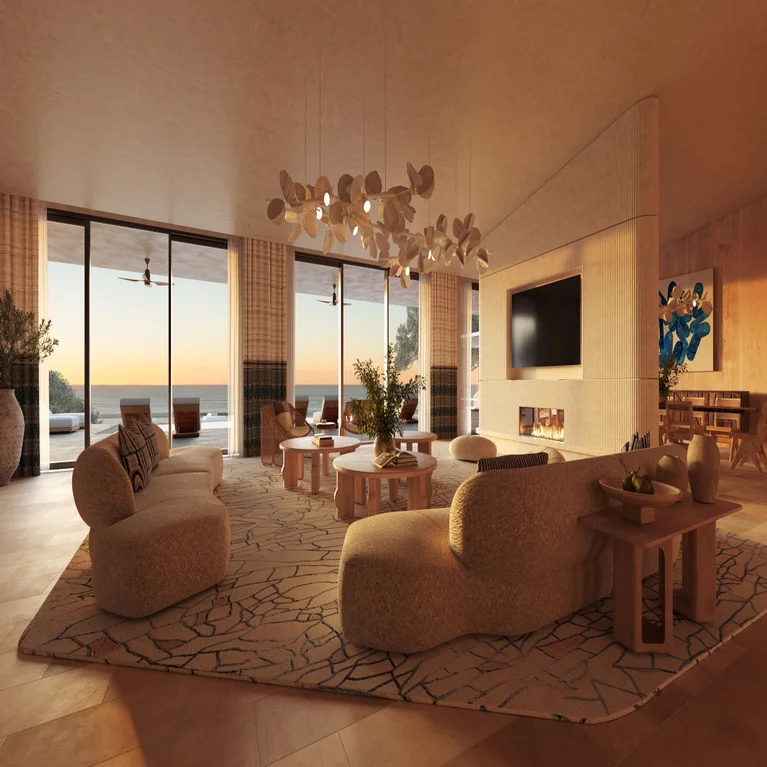Living area with curved sofas, large windows overlooking the ocean at sunset, neutral palette, low-profile TV, minimalist fireplace, and soft ambient lighting.