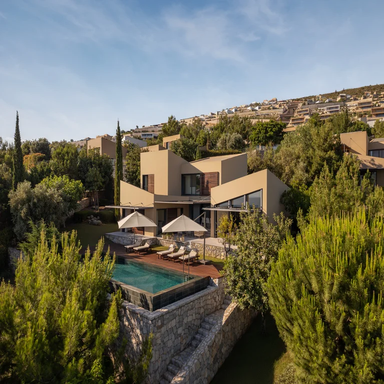 Eco-inspired retreat featuring a tranquil pool area, accessible seating, shaded spaces, and views of verdant hills with distant residences beneath a clear sky.