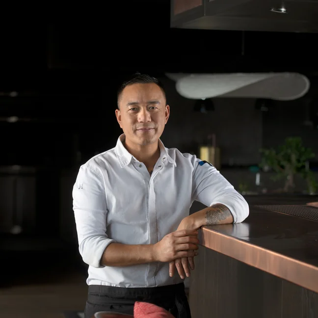 A guest in a light shirt stands by a dark wooden counter with hands resting on the surface. Soft lighting creates a calm, welcoming atmosphere in the contemporary interior.