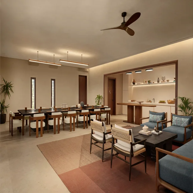 Calm space with natural wood tables, chairs, sofas and greenery. Open kitchen and soft lighting complement the neutral, minimalist decor. Accessible layout for all guests.