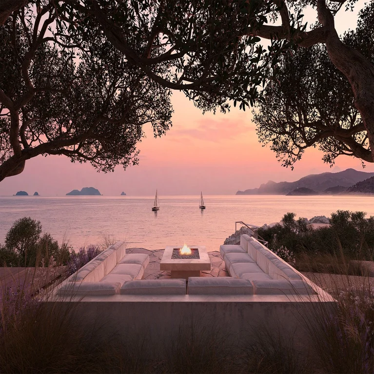 Outdoor seating area with fire pit faces the sea at sunset, surrounded by trees. Sailboats and islands are visible on the horizon, designed for comfort and connection to nature.