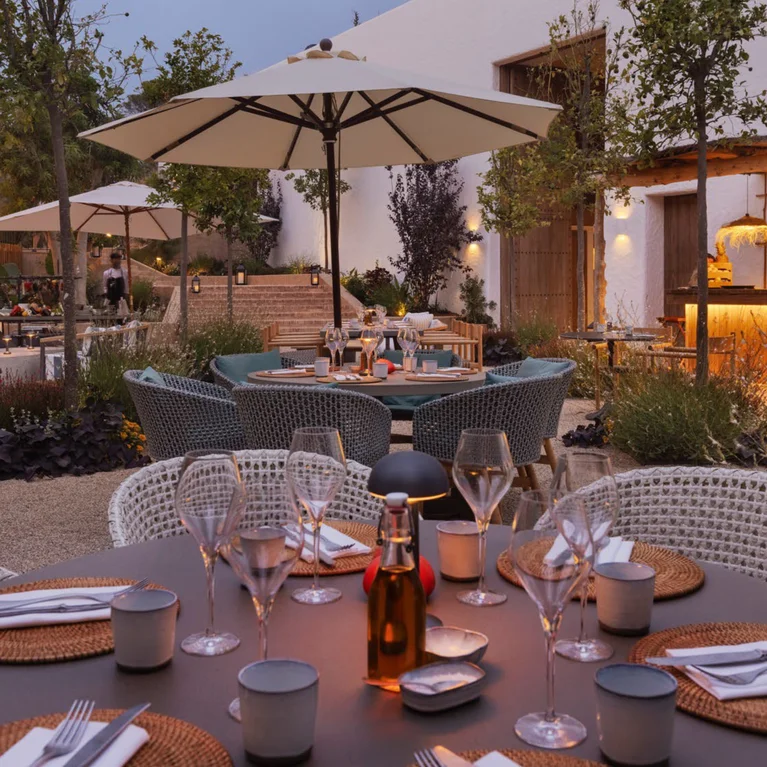 晚间用餐区摆放着餐桌,使用可持续材料、遮阳伞以及来自酒吧和邻近建筑的柔和灯光。提供无障碍座位。.