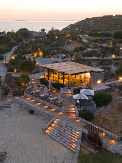 Beachside restaurant with outdoor seating, native greenery, and gentle path lighting, offering views of the sea at dusk. Accessible pathways support ease of movement.