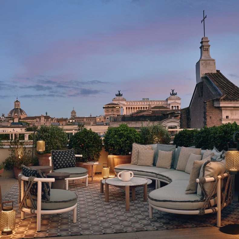 Terrasse avec des sièges confortables, une végétation abondante, un éclairage doux et des vues sur les bâtiments historiques et les dômes sous un ciel nocturne chaud.