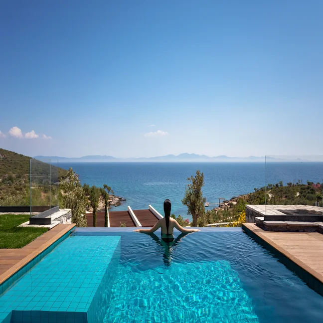 An infinity pool overlooking the sea with distant mountains and a clear blue sky, highlighting tranquil natural surroundings and mindful design.