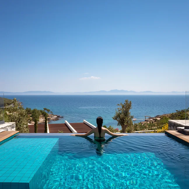 An infinity pool overlooking the sea with distant mountains and a clear blue sky, highlighting tranquil natural surroundings and mindful design.