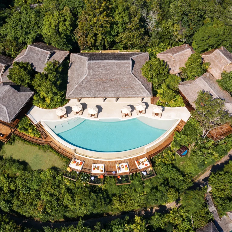 弧形泳池边上是绿树成荫的木质结构,池边还贴心地摆放着躺椅和遮阳伞。.