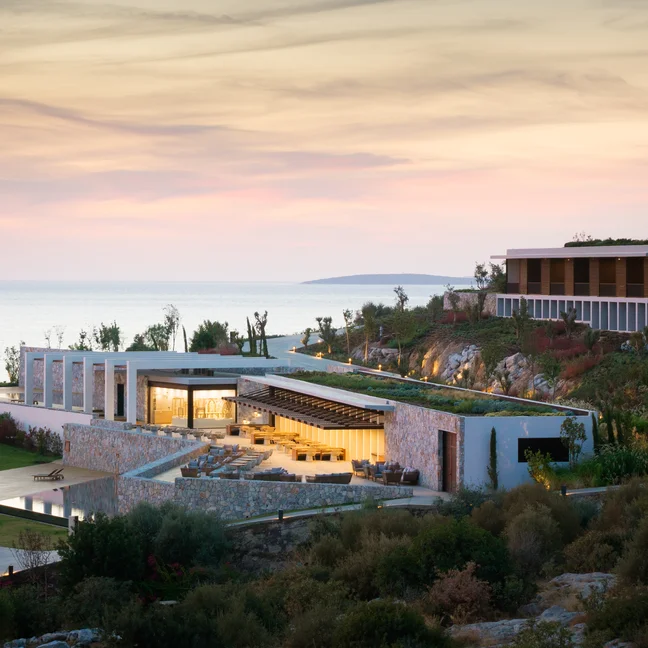 Contemporary buildings with landscaped gardens and gentle lighting face a calm sea, reflecting Six Senses’ focus on wellness and sustainability.