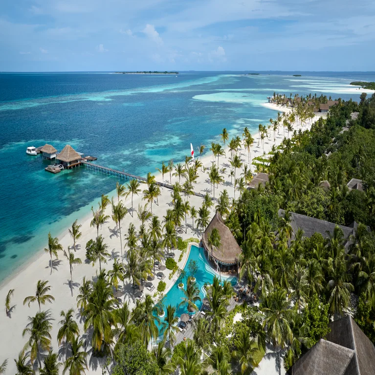 Palm trees, a pool, white sand, turquoise ocean water, and sustainably built wooden villas set along the shoreline at a beachfront resort.