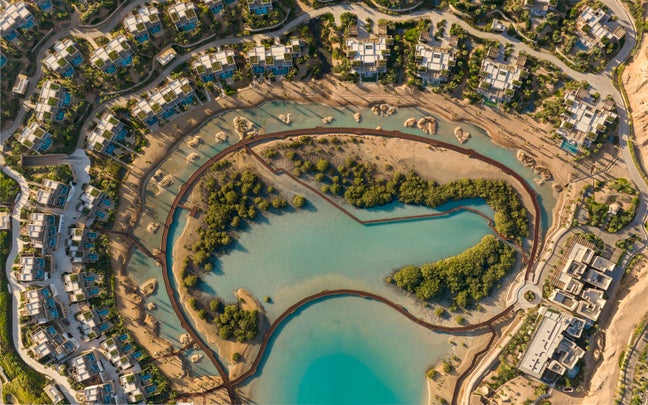 Turquoise lagoon with small islands, bordered by contemporary buildings and curved roads, set within sandy natural surroundings.