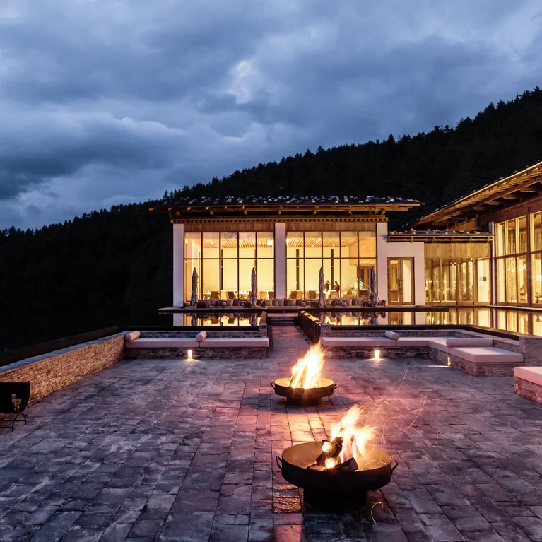 湖畔度假村拥有宽阔的落地窗,黄昏时分庭院火盆的灯光柔和,周围是森林覆盖的山丘和阴霾的天空。.
