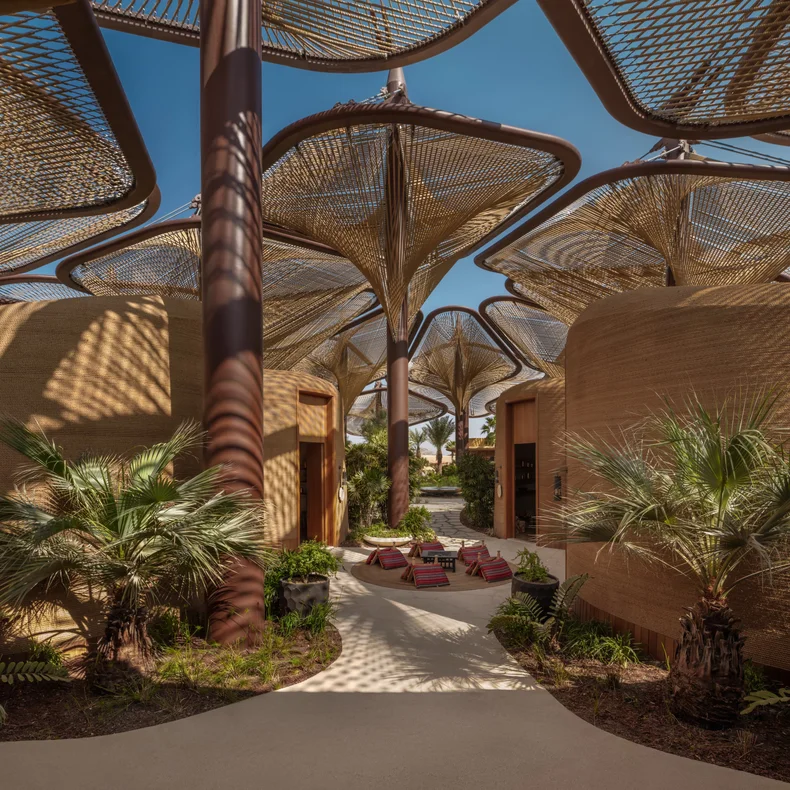 Spacious plaza features woven canopies, curved architecture, palm trees, and lounge seating, designed for comfort and shaded relaxation beneath a clear blue sky.