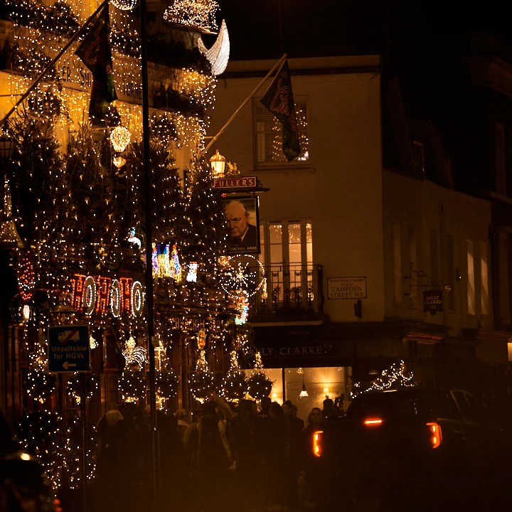 The Churchill Arms pub at night, adorned with numerous illuminated Christmas trees and festive lighting.