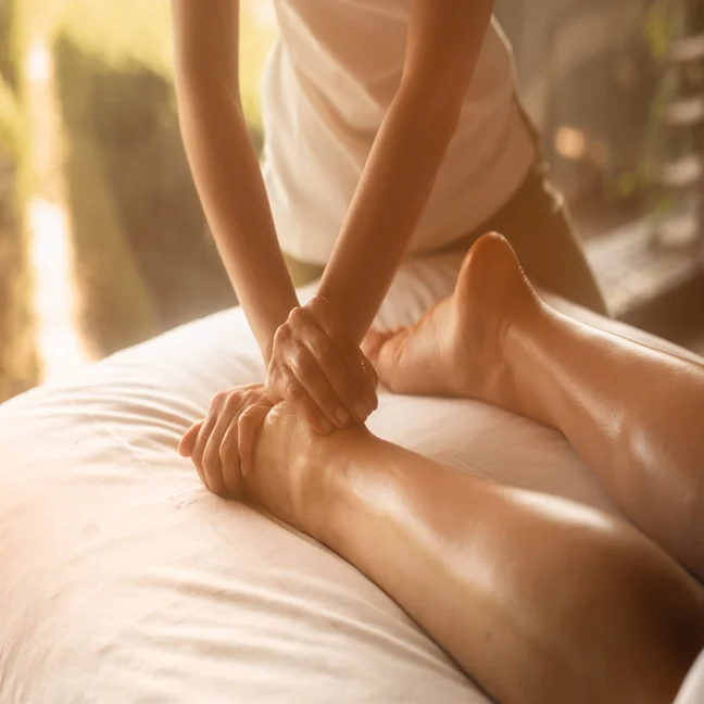 A therapist gently massages a guest’s leg in a serene wellness space, lit softly to support relaxation and holistic rejuvenation.