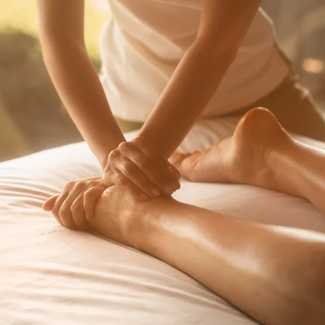 A therapist gently massages a guest’s leg in a serene wellness space, lit softly to support relaxation and holistic rejuvenation.