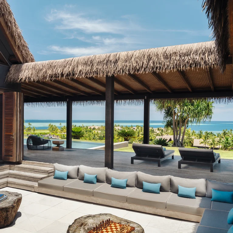 别墅配有茅草屋顶、面向棕榈树和大海的遮阳露台,以及带灰蓝色坐垫的下沉式座位区,让您享受轻松惬意的户外生活。.