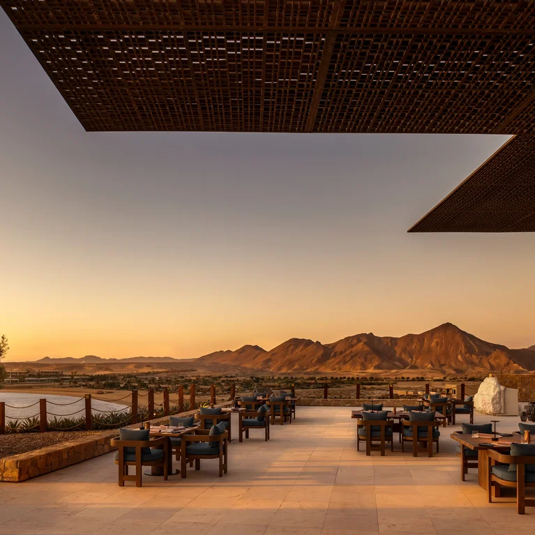 Restaurant terrace with orderly tables and chairs, offering views of mountains and water under a clear sky. Accessible pathways ensure comfortable navigation.