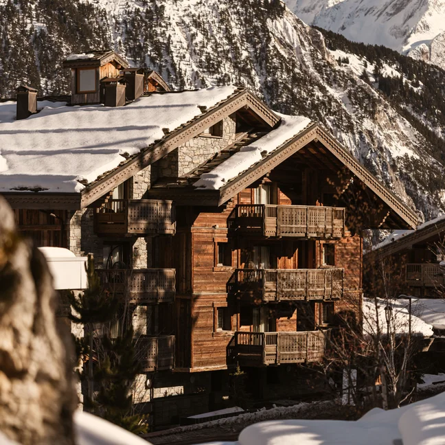 一座多层、带阳台的木屋,在白雪皑皑的群山映衬下,整座房屋都被积雪覆盖。.
