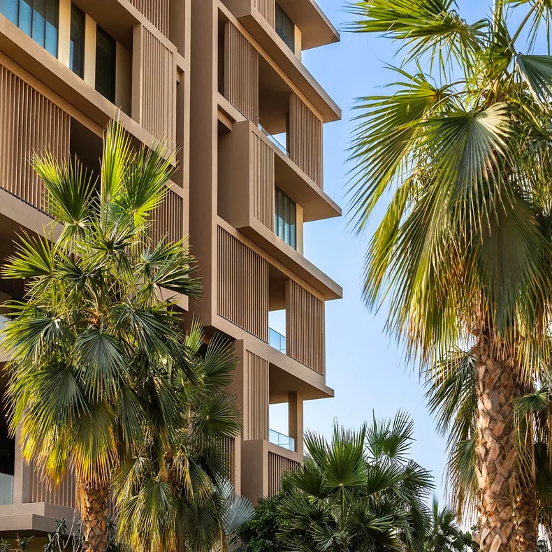 Contemporary building featuring spacious outdoor terraces and vertical wooden elements, framed by palm trees against a bright sky.