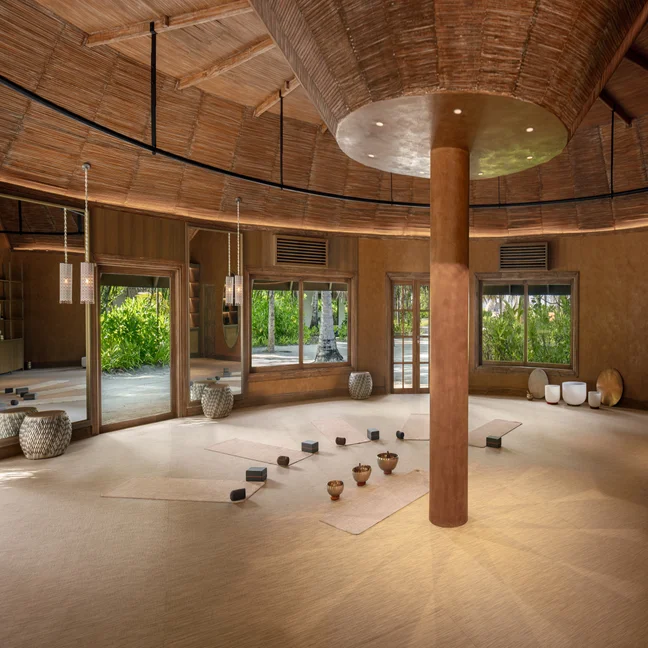 Yoga studio with natural woven flooring, mats, blocks, and bowls. Large windows offer garden views and fill the serene space with natural light.