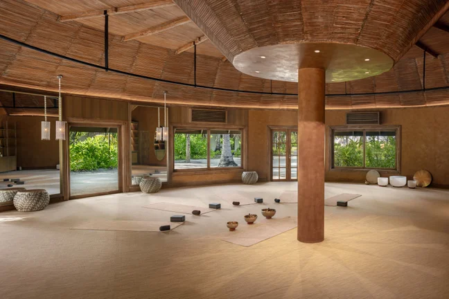 Yoga studio with natural woven flooring, mats, blocks, and bowls. Large windows offer garden views and fill the serene space with natural light.