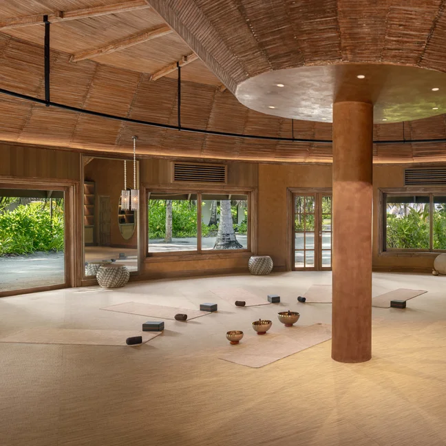 Yoga studio with natural woven flooring, mats, blocks, and bowls. Large windows offer garden views and fill the serene space with natural light.