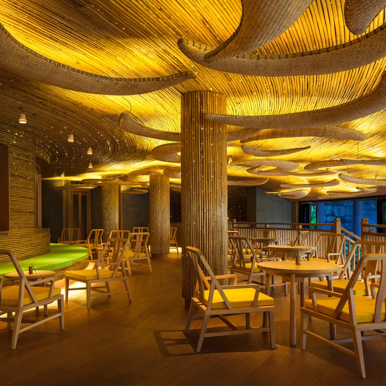 L'intérieur du restaurant est composé de meubles en bois naturel, d'un éclairage doux et doré et d'un plafond en bois ondulé pour créer un espace de restauration accueillant et contemporain.