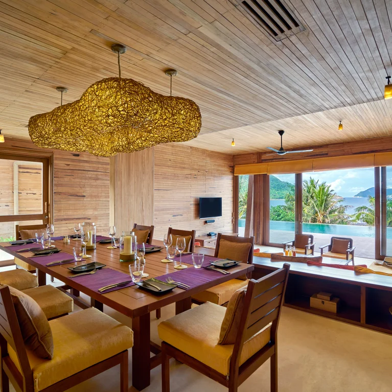用餐区配有天然木质表面、有机形状的吊灯、餐桌、嵌入式窗凳,以及棕榈树和远山的美景。.