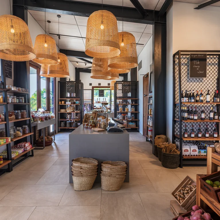 Grocery store with woven pendant lighting, wooden shelving filled with food items, floor baskets, and neatly arranged fresh fruits and vegetables.