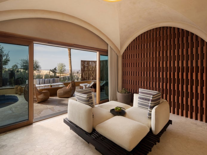 Lounge area featuring cushioned chairs, a brown accent wall, curved ceiling, and sliding doors leading to a patio with wicker seating and a compact pool.