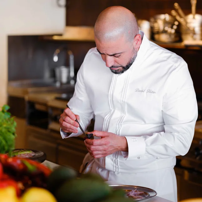 Un experto culinario prepara un plato en una cocina moderna, utilizando productos frescos de temporada que se exponen en la parte delantera del espacio de trabajo.