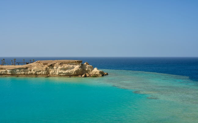 Cliffside landscape with palm trees rises above turquoise water, meeting deeper blue ocean beneath a clear sky, reflecting natural beauty and tranquility.
