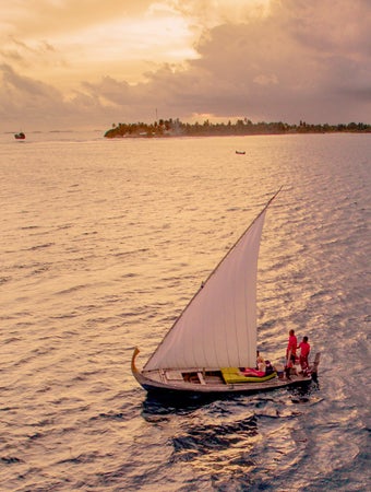曇り空の下、島の近く、夕暮れの穏やかな海を進む白い帆を張ったヨット。.
