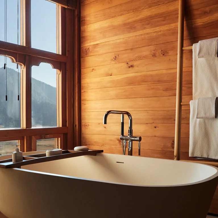 木质浴室内的浴缸,透过大窗户可饱览山景。浴缸旁的木梯上铺着白色毛巾。.