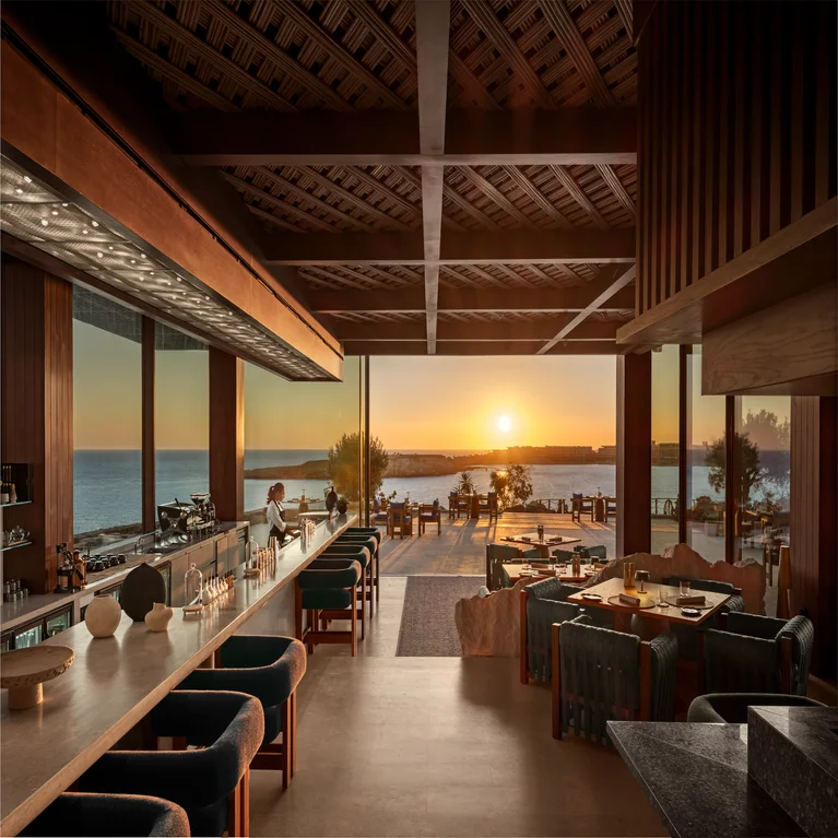 Restaurant and bar feature ocean views at sunset, wooden details, natural light, and inviting seating for a serene dining atmosphere.