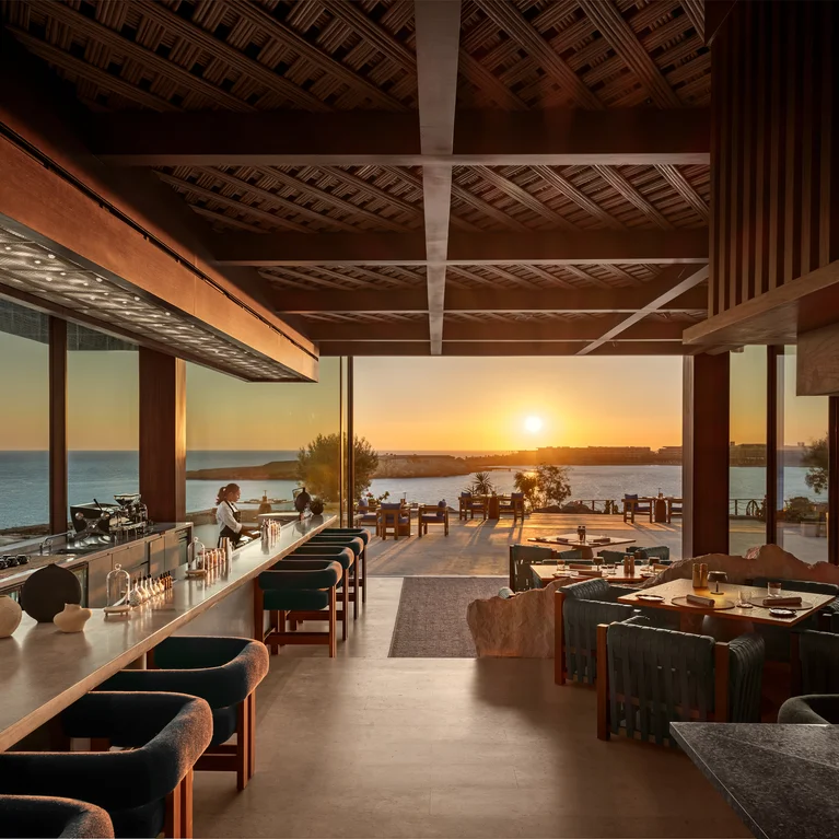 Restaurant and bar feature ocean views at sunset, wooden details, natural light, and inviting seating for a serene dining atmosphere.