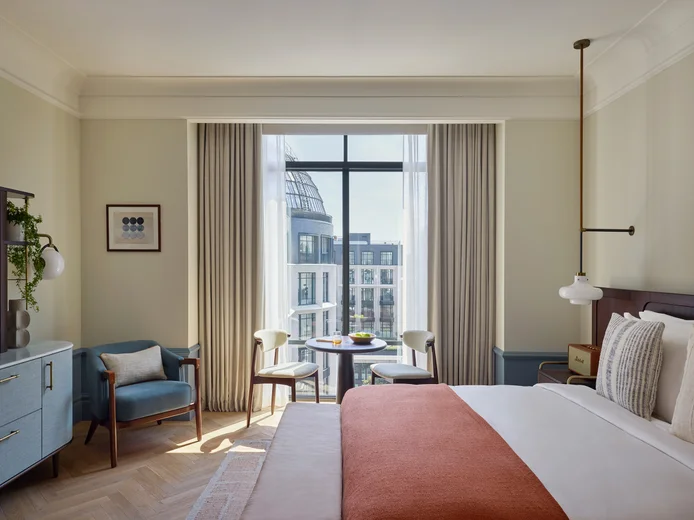 Thoughtfully designed room featuring a king bed, organic textile accents, seating by large windows, and urban city views beyond sustainable furnishings.