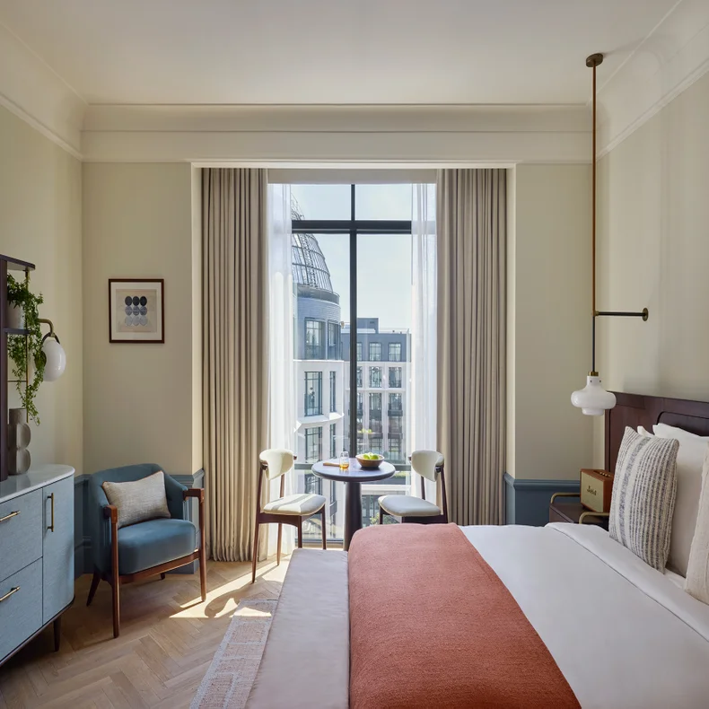 Thoughtfully designed room featuring a king bed, organic textile accents, seating by large windows, and urban city views beyond sustainable furnishings.