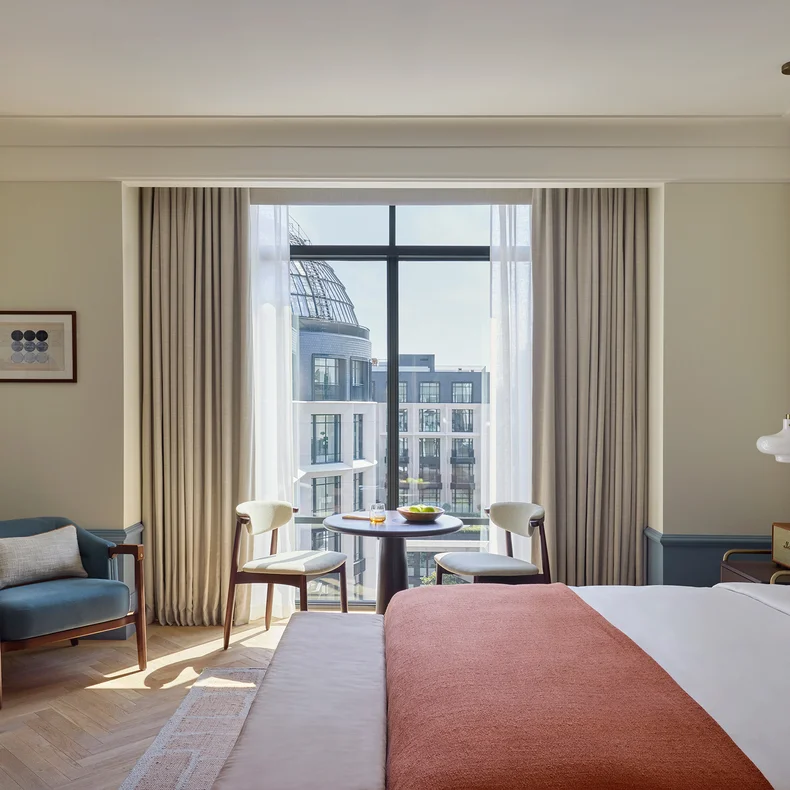 Thoughtfully designed room featuring a king bed, organic textile accents, seating by large windows, and urban city views beyond sustainable furnishings.