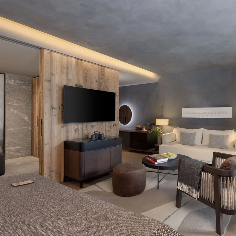 Tranquil room featuring a large bed, comfortable seating, integrated TV, bath, natural wood details and expansive window with sheer curtains that welcome soft daylight.