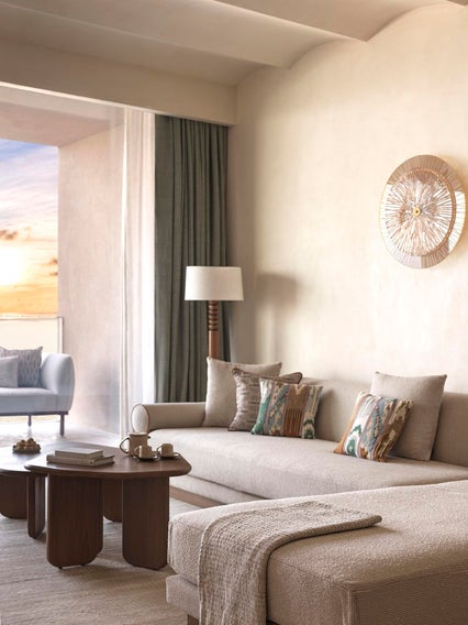 Beige sofa with patterned pillows, wooden coffee table, floor lamp, and wall art. Sliding glass doors open to a balcony overlooking the sunset. Space is accessible and welcoming.