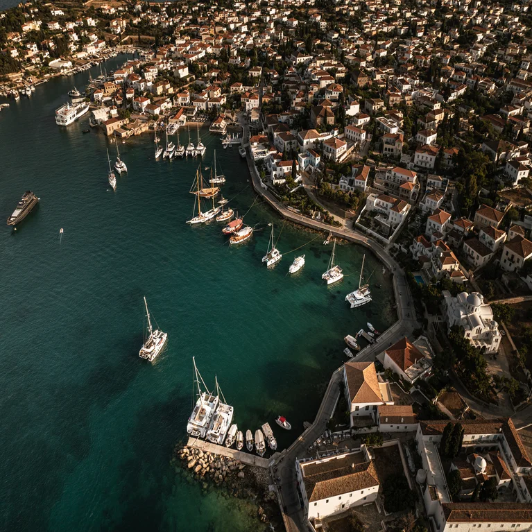 Coastal town marina with yachts and sailboats in calm waters, bordered by shoreline homes and buildings, emphasizing harmony between ocean and community.