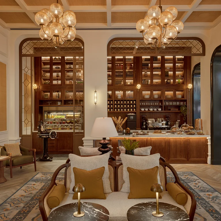 Inviting lobby with soft lighting, comfortable seating, marble tables, accessible wooden bar featuring visible pastries and drinks. Warm tones and clear pathways throughout.