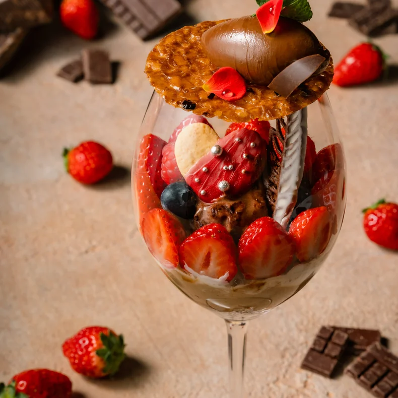 グラスにイチゴ、ブルーベリー、チョコレート、ウエハースを重ね、軽い表面に置き、近くに新鮮なイチゴとチョコレートのかけらを並べる。.