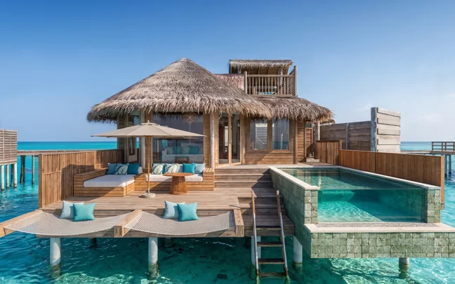 A villa over the water featuring a private pool, wooden deck, sun loungers, and hammock nets suspended above the sea.